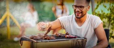 Umweltfreundlich grillen: Unsere Tipps. Das Bild zeigt einen jungen Mann, der Fleisch auf einem Holzkohlegrill grillt.