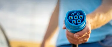 Das Bild zeigt, wie ein Mann den Ladestecker für ein Elektroauto in die Kamera hält.