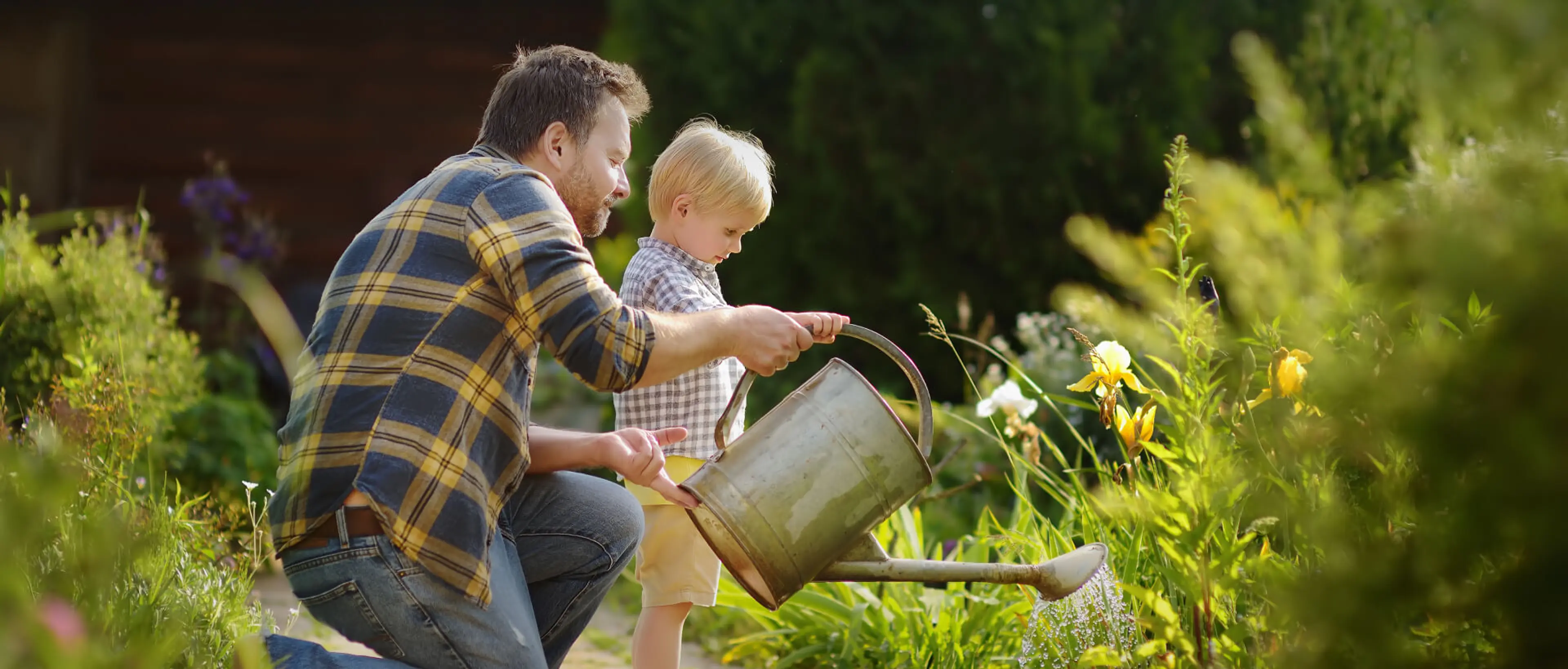 Nachhaltig gärtnern: Wasser, Geld und Zeit sparen. Das Bild zeigt einen Vater mit seinem kleinen Sohn beim Gießen eines Beetes mit einer Gießkanne.