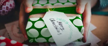 Nachhaltige Geschenke: 10 grüne Geschenkideen. Das Bild zeigt zwei Hände, die ein eingepacktes grünes Geschenk mit der Aufschrift "Merry Christmas" halten.