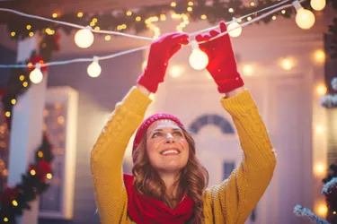 LED-Lichterketten benötigen mehr als 80 Prozent weniger Strom als Lichterketten mit herkömmlichen Glühlämpchen. Das Bild zeigt eine lächelnde Frau. Sie schaut nach oben und befestigt eine LED-Kugel-Lichterkette.