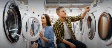 Ab März 2021 gibt es das neue Energieeffizienzlabel. Das Bild zeigt zwei junge Menschen, die Wäsche in einer Waschmaschine waschen.