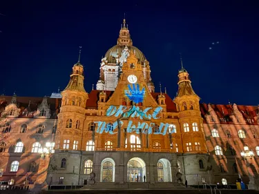 Dieses Bild zeigt das neue Rathaus Hannovers, welches orange angestrahlt wurde. Zudem wurde der Schriftzug "Stoppt Gewalt gegen Frauen" in blau auf das Gebäude projiziert.