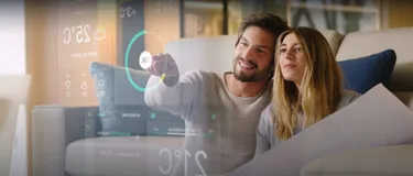 Heizkosten sparen: Ratgeber mit einfachen Tipps. Das Bild zeigt ein junges Paar, das ein modernes Smart Home System bedient und die Temperatur für die Heizung einstellt.