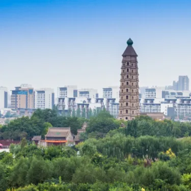 Yinchuan. Dieses Bild zeigt einen Ausschnitt der Stadt Yinchuan in China. Dort sind viele Bäume im Vordergrund, sowie viele Hochhäuser im Hintergrund zu sehen.