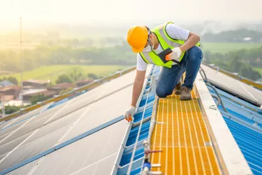Photovoltaik. Dieses Bild zeigt einen Monteur, der auf einem Dach eine Photovoltaikanlage befestigt.
