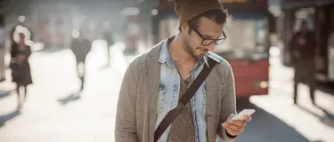 Grün und vernetzt. Dieses Bild zeigt einen Mann, der eine Mütze und Brille trägt und nach unten auf sein Smartphone schaut.
