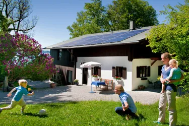Investition in die Zukunft: Das Bild zeigt ein Haus mit moderner Solaranlage mit einer jungen Familie im Vordergrund