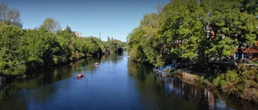 Dieses Bild zeigt einen breiten Fluss, auf dem mehrere Menschen auf Kanus und Booten unterwegs sind.