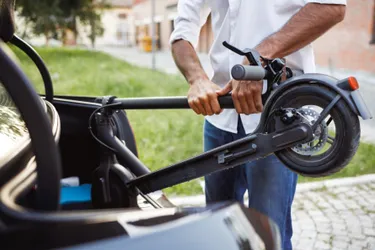 Elektroscooter für innerstädtische Pendler. Das Bild zeigt einen Mann, der einen E-Scooter zusammenfaltet und in Kofferraum legt.