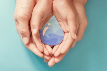 Trinkwasserqualität. Dieses Bild zeigt vier Hände, zwei größere außen und zwei kleinere innen. Die Hände halten einen gezeichneten Wassertropfen.