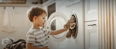 Nachhaltig & umweltfreundlich Wäsche waschen: Das Bild zeigt ein Kind, das einen Teddybären in die Waschmaschine legt.