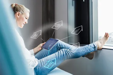 Haustechnik. Dieses Bild zeigt eine Frau am Tablet. Aus dem Tablet kommen verschiedene Symbole für Themen wie Lautstärke, Strom, WLAN.