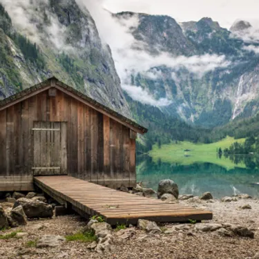 Besonders klimaschonend sind Urlaubsziele in der Nähe. Das Bild zeigt eine Hütte am Obersee inmitten von Bergen bei Nebel.