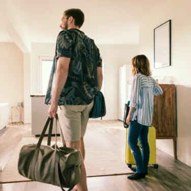 Wer umweltfreundlich reisen möchte, sollte nachhaltige Unterkünfte buchen. Das Bild zeigt ein Paar mit Koffern, das in einer Urlaubsunterkunft ankommt.