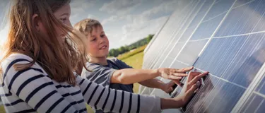 Solarenergie. Dieses Bild zeigt ein Mädchen un deinen Junden, die beide eine Solarzelle anfassen.