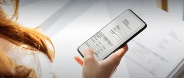 Die Strompreis-Zusammensetzung einfach erklärt. Das Bild zeigt, wie eine Person ein Handy in der Hand hält. Es ist eine Stromrechnung auf dem Handy mit verschiedenen Positionen und Beträgen zu sehen.