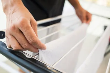 Feuchte Handtücher oder Laken senken die Raumtemperatur. Dieses Bild zeigt den Ausschnitt eines Wäscheständers, auf den gerade ein nasses Handtuch gehängt wird.