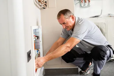 Ein Heizungsmonteur installiert in einem Heizungskeller die Inneneinheit einer Wärmepumpe