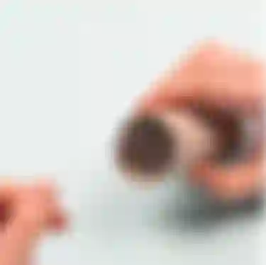 Kinderhände beim Basteln, die eine Schnur durch vier Löcher in einer Klopapierrolle ziehen