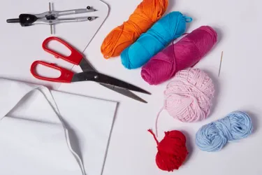 Materialien für DIY Pompons: Das Bild zeigt Schere, Wollreste, Zirkel, Sticknadel und Pappe.