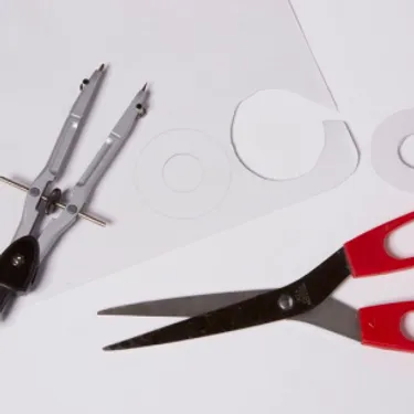 Schritt 1: Das Bild zeigt, wie auf Pappe Schreiben mithilfe eines Zirkels und einer Schere ausgeschnitten werden. 