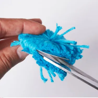 Schritt 3: Das Bild zeigt, wie ein Pompon-Rohling mit einer Schere zugeschnitten wird.