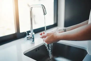 Close-up zweier Hände, die in einer Spüle unter fließendem Wasser gewaschen werden