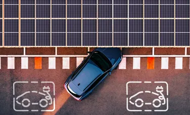 Ansicht eines Autos das unter einem mit Solarpaneelen gedeckten Carport einparkt aus der Vogelperspektive