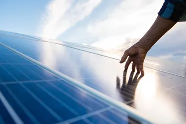 Nahaufnahme einer Hand, die über die Solarpaneele einer PV-Anlage streicht