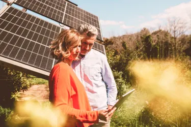 Eine Frau und ein Mann stehen vor einer im Garten installierten PV-Anlage und kontrollieren deren Ertrag auf einem Tablet
