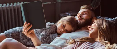 Junge Familie kuschelt vor der Heizung und liest ein Buch