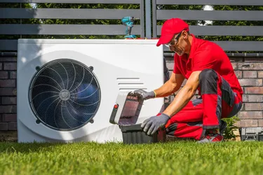 Ein Handwerker kniet neben einer in einem Garten stehenden Wärmepumpe