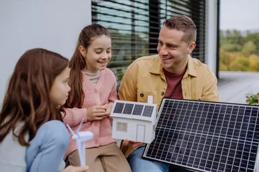 Ein junger Vater erklärt seinen Töchtern die Vorteile erneuerbarer Energien und hält dabei ein kleines Photovoltaikmodul in der Hand