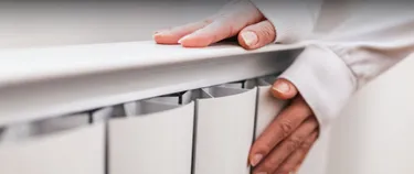 Eine Person legt ihre Hände auf eine Heizung.