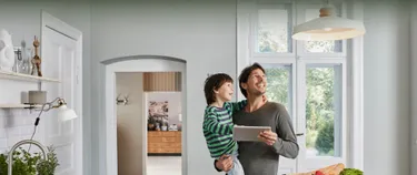 Mann mit Jungen auf dem Arm kontrolliert Energieverbrauch per Tablet