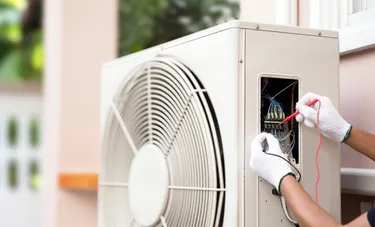 Nahaufnahme einer Wärmepumpe an der das behandschuhte Händepaar eines Monteurs gerade die elektrische Spannung misst