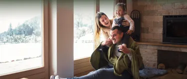 Eine Familie mit Decke vor dem Fenster, dahinter eine Winterlandschaft.