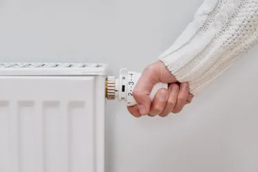 Nahaufnahme einer Frauenhand die am Thermostat einer Heizung dreht