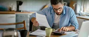 Junger Mann prüft Gasrechnung mit Taschenrechner in seiner Küche