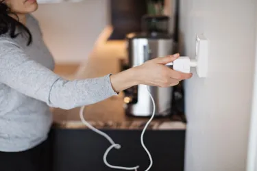 Eine Frau steckt das Ladekabel ihres Handys in eine in der Wand ihrer Küche befindliche Steckdose.