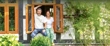 Petra und Mathias von Elling sitzen auf der Fensterbank ihres Hauses und schauen in ihren Garten.
