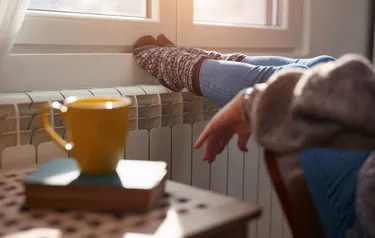 Das Foto zeigt die Füße einer in einem Sessel sitzenden Person, die an einem Heizkörper gewärmt werden