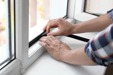 Nahaufnahme zweier Männerhände beim Abkleben einer Dichtung für den Fensterrahmen.