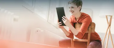 Eine Frau sitzt vor der Heizung und schaut auf ein Tablet