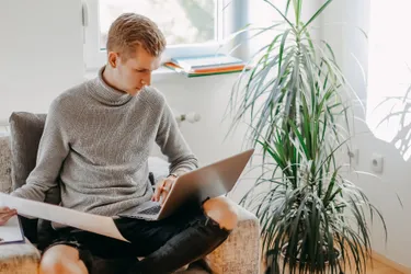 Ein junger Mann vergleicht ein Schreiben, das er in der Hand hält mit Angaben, die er auf seinem Laptop abliest