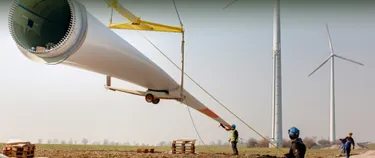 Drei Bauarbeiter bewegen ein riesiges Rotorblatt eines Windrads mit Hilfe eines Krans.