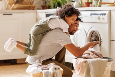 Ein Vater befüllt eine Waschmaschine und trägt dabei seinen Sohn huckepack