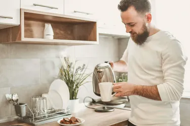 Ein Mann gießt Wasser aus einem Wasserkocher in einen Kaffeebecher