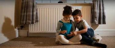 Zwei Kinder spielen im Wohnzimmer und halten ein Tablet in der Hand.